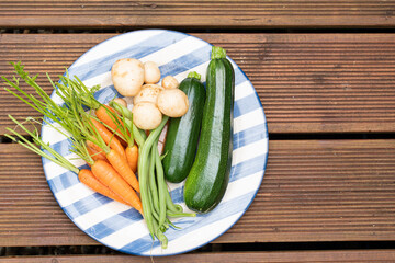 Home grown vegetables carrots courgettes beans and potatoes on a blue striped plate on rustic brown...