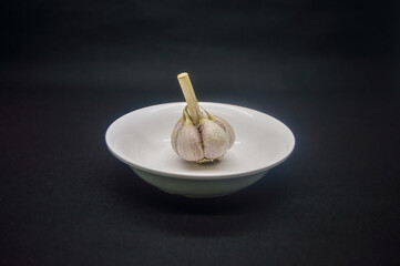 a garlic on a plain white plate isolated on a plain black background