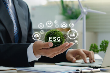 Businessman hand holding green earth with ESG environment social governance investment business concept.Using a computer to analyze ESG for sustainable organizational development.