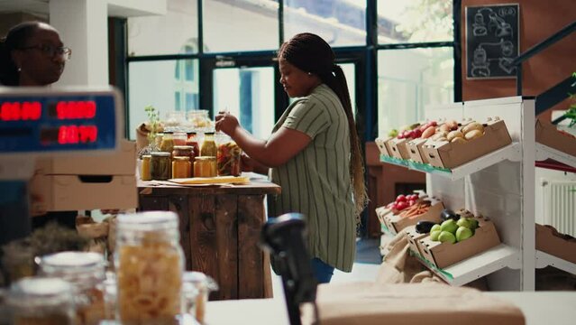 African american client pouring various bulk products from jars, buying organic homemade merchandise stored in reusable containers. Vegan woman choosing bio items at market. Handheld shot.
