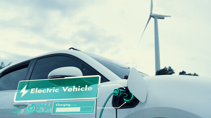 Electric car recharging energy from EV charging station display futuristic smart battery status hologram by EV charger plug cable in wind turbine farm. Alternative clean energy sustainability. Peruse