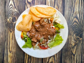 Gado Gado is an Indonesian mixed salad with peanut sauce and vegetables such as lettuce, tomatoes, cabbage, beans, potatoes, tomatoes, and red onions. Add crackers, tempeh, tofu, and rice cake