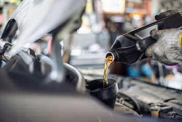 Close-up of a mechanic's gloved hands pouring new motor oil into a vehicle during a service check..