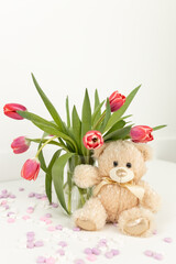 Background for Valentine's Day. Assorted pink and white heart shaped candies with printed messages of love, pink tulips and beige cute Teddy bear on a white background. Gift for Women's Day, March 8