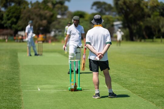 a local cricket match being played on a green cricket oval in summer in australia. australian cricketer batting and bowling in a game