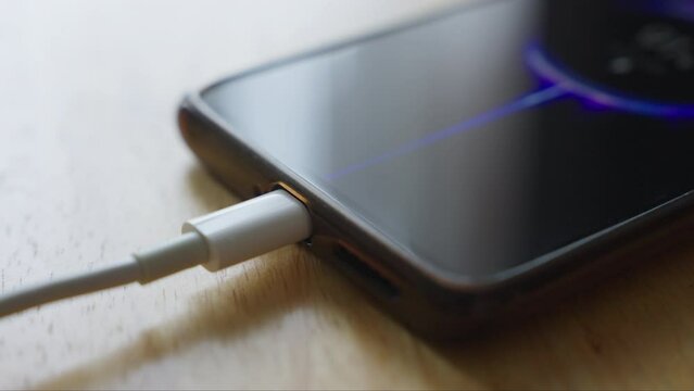 Closeup view of mobile smart phone charging battery on wooden desk. Plug in the charger USB C. Charger device process
