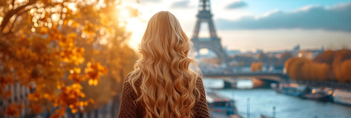 A beautiful slim girl with long blond hair standing in front of the Eiffel Tower in Paris. - obrazy, fototapety, plakaty