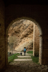 Fototapeta na wymiar Young woman walking with dog and sightseeing in the medieval hermitage of Tobera