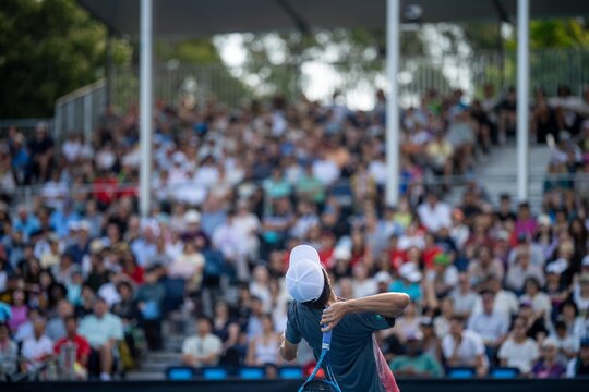 playing tennis on a blue tennis court. serving in a tennis with a crowd of fans watching in australian open