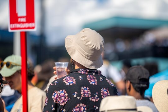 Tourist with backpacks in a crowd watching a sporting event in a stadium. Sports fans cheering and watching tennis at the Australian open in Australia. Hot summer sport fans, wearing summer clothes.
