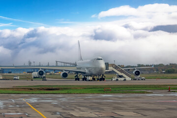 Large cargo plane parking preparation for flight loading food and goods. Large clouds of fog in the background