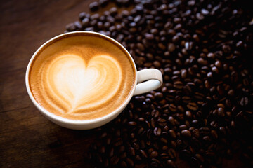 Cup of coffee latte with heart shape and coffee beans on old wooden background, with copy space.
