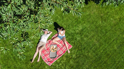 Female friends eating pizza on summer picnic in park, relaxing on grass and having fun, aerial...
