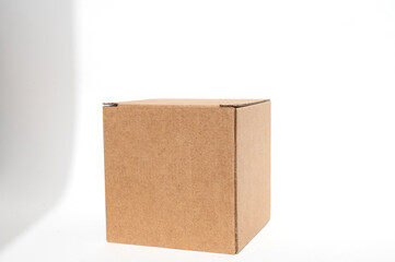 A brown square box made of corrugated cardboard on a white background with a shadow from the window.