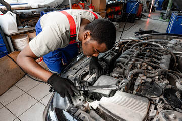 Young African auto mechanic checking car engine under the hood in auto service