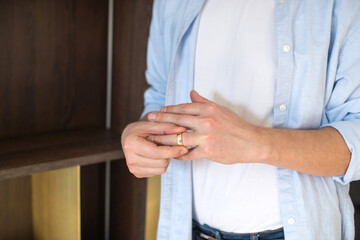 A man removes a gold wedding ring from his left hand ring finger - obrazy, fototapety, plakaty