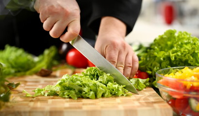 Naklejka na ściany i meble Cook holds knife in hand and cuts on cutting board green for salad or fresh vegetable soup with vitamins. Raw food and vegetarian recipe book in modern society popular concept.