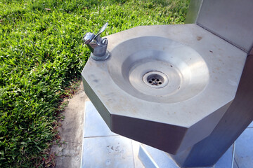 aluminium drinking fountain on tile base with green grass lawn under sunlight