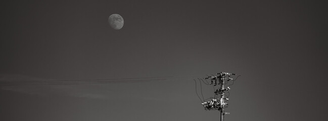 Black and white image of the moon above power lines panoramic 