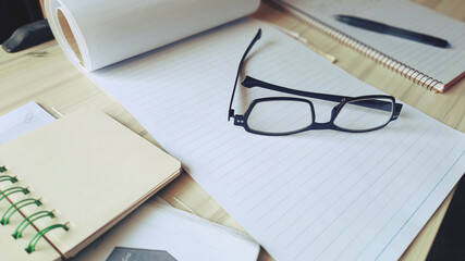 A messy desk with notepads, glasses, pens, study and work concepts.
