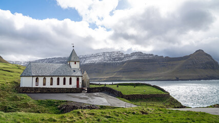 Vidareidi village church surrounded by sweeping panoramas of hills and north Atlantic Ocean, Faroe...