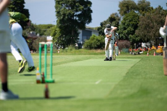cricketer batting on a cricket pitch, a local cricket match being played on a green cricket oval in summer in australia