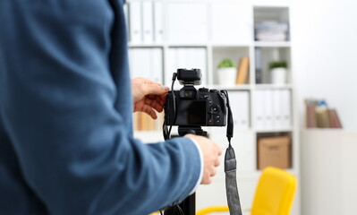 Male arms in suit mount camcorder to tripod making promo videoblog or photo session in office...