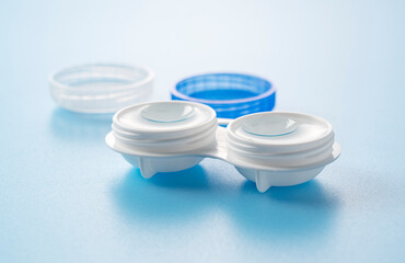 A case of contact lenses and soft contact lenses placed against a blue background.