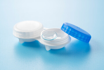 A case of contact lenses and soft contact lenses placed against a blue background.