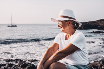Carefree satisfied senior woman with white hat looking at new day from sea beach at sunrise...