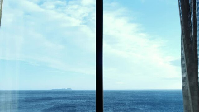 Open curtain with the view of seascape and cloud sky.