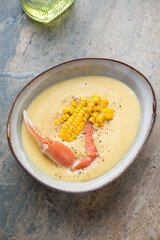 Bowl of crab and corn soup, vertical shot on a beige and grey granite background, elevated view