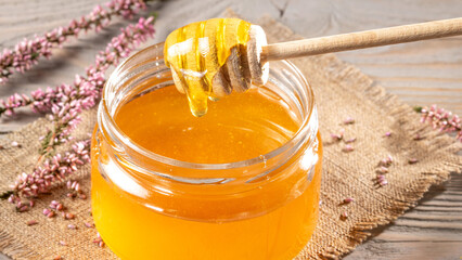 Jar of heather honey and honey stick on rustic tabletop - natural sweetener concept. Close up
