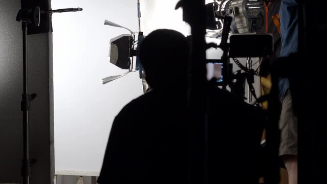 Behind the scenes of busy filming or video production in studio and busying film crew team working in set which include pro equipment such as film lights and big light diffuser. Handheld footage style