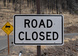 Road closed sign with curve and burnt forest in background.   Close-up.