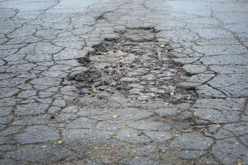 A large hole in the asphalt with cracks on the road. Close-up. Background. Space for text.