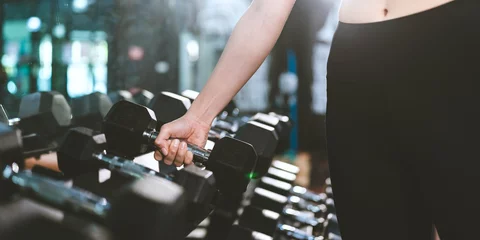 Afwasbaar Fotobehang Fitness Close up of Confident muscular Asian athlete female is lifting a dumbbell in gym or fitness to build up her body and muscle. Wellbeing, wellness of city people lifestyle, Serious and effort work out.