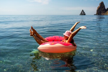 Summer vacation woman in hat floats on an inflatable donut mattress. Happy woman relaxing and enjoying family summer travel holidays travel on the sea.