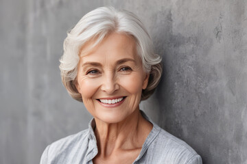 Portrait of beautiful older woman smiling and standing by gray wall. A place for text, a banner for advertising.