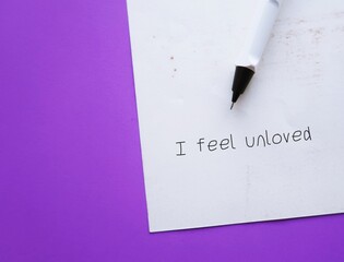 On purple background, pen wrote on a note I FEEL UNLOVED - pain of feeling unloved or feel left alone in a relationship group of friends