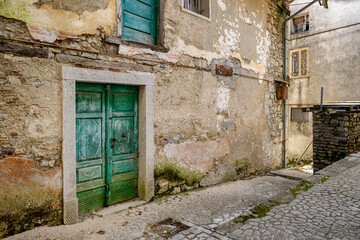 Fototapeta na wymiar Vintage green front door facing on an alley of an almost abandoned Italian mountain village. Canalaz, Grimacco, Udine province, Friuli Venezia Giulia, Italy. Urbex photography.