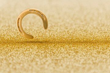 Golden horseshoe on golden glitter background with shiny bokeh effect.