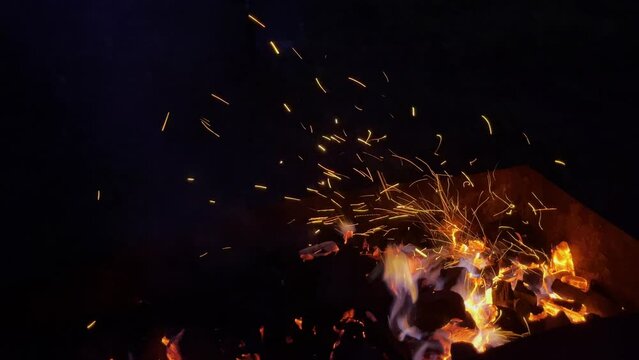 Closeup handheld shot of sparks blazing from burning coal in fire pit at dark room