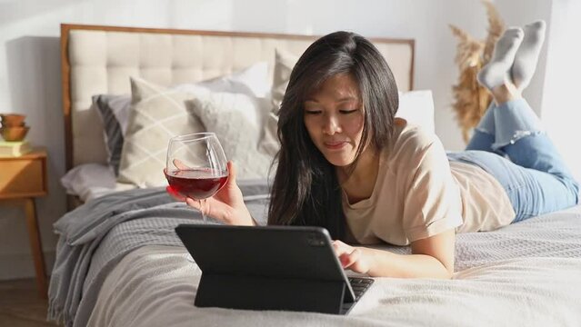 Happy beautiful woman in casual clothes talking on video call on digital tablet lying on the bed. Work from home education online. Playing game shopping online relaxing