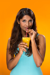 Indian woman drinking orange juice on colorful background