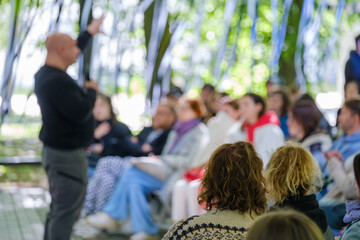 Engaged audience listening to a speaker at an informal outdoor workshop surrounded by nature.