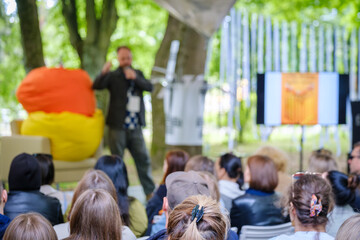 Informal outdoor event with a dynamic speaker engaging with a diverse audience seated in a park.