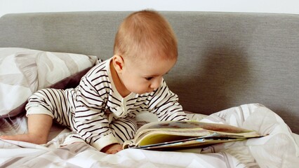 A cute little baby boy is carefully looking at a book with interest