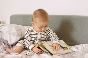 A cute little baby boy is carefully looking at a book with interest