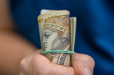 Zwiniete w rulon polskie pieniądze trzymane w dłoni, dużo banknotów pln
